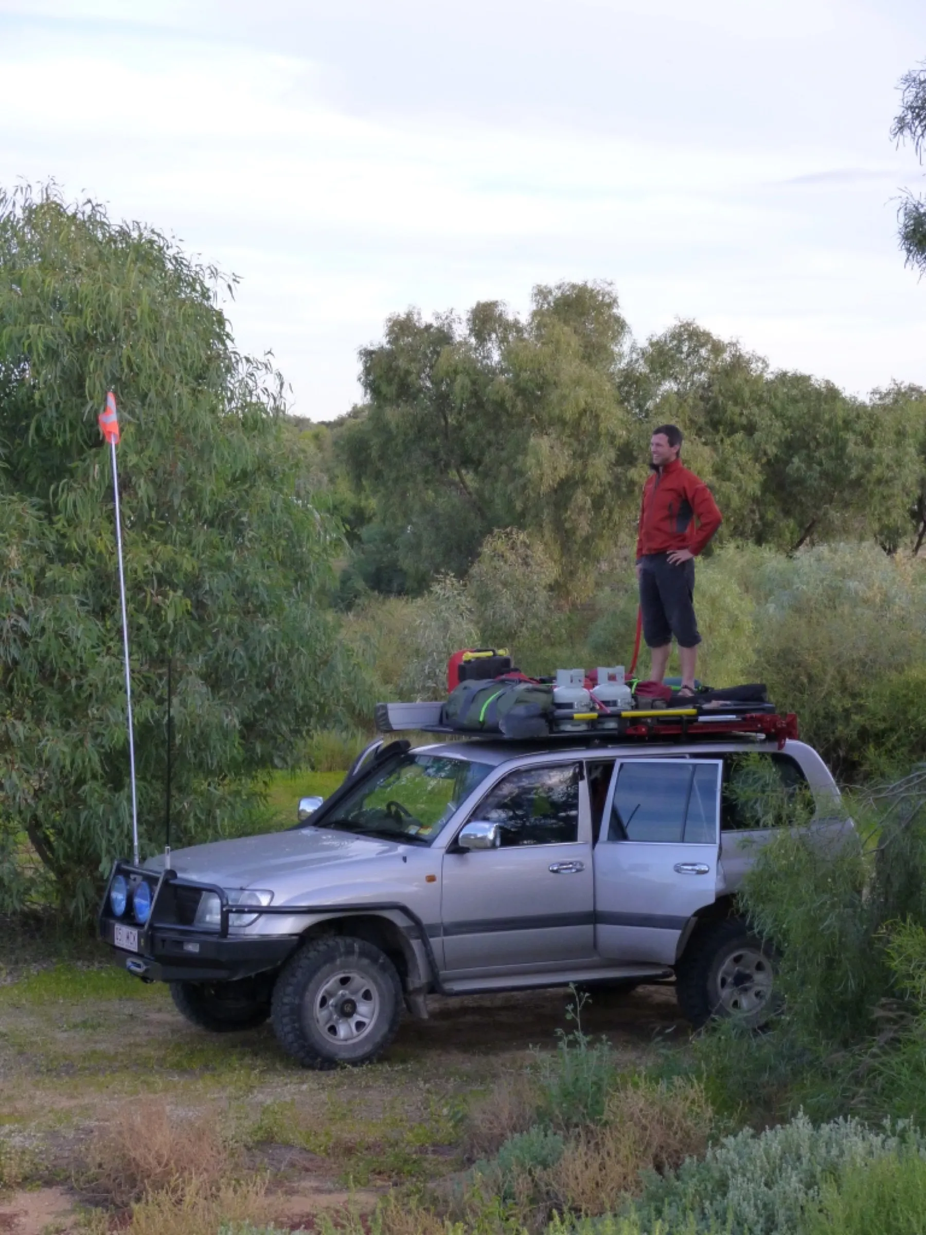 Andrew standing on the roof rack of a Land Cruiser among outback gum trees
