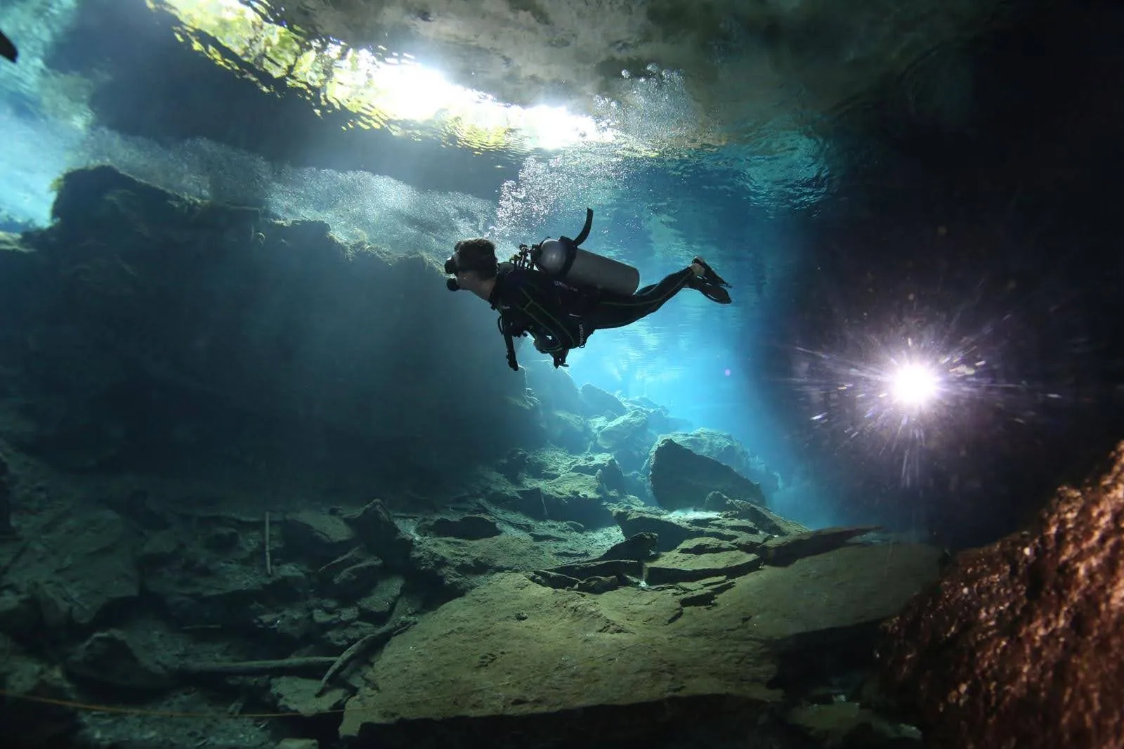 A scuba diver silhouetted in a sunlit underwater cave
