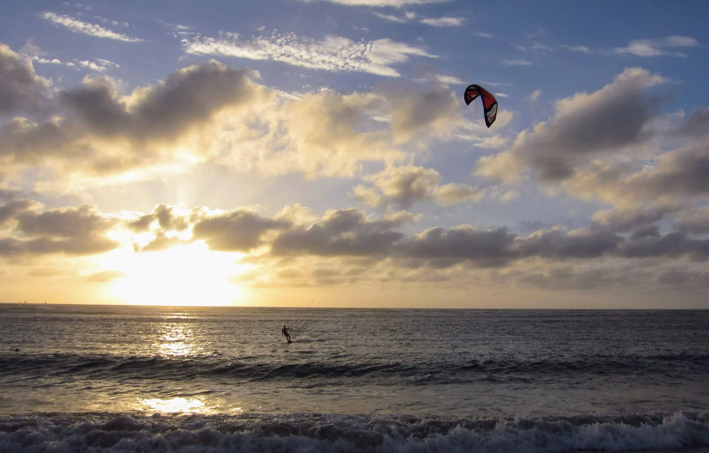 A kitesurfer on the sea at sunset under scattered cloud